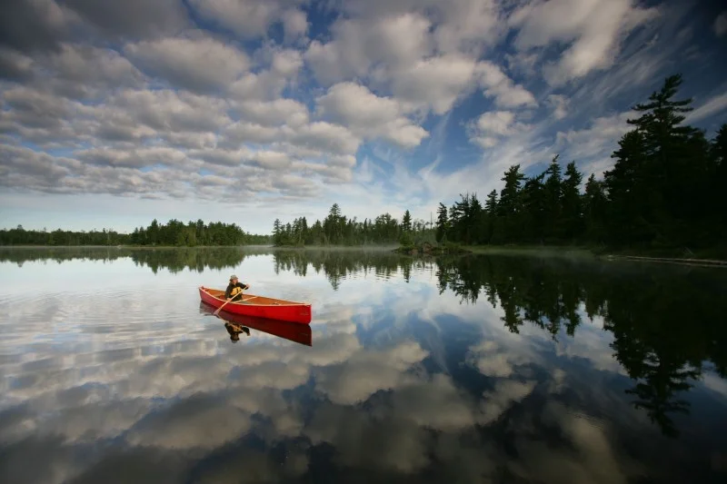 A red canoe on a still Quetico lake at dawn